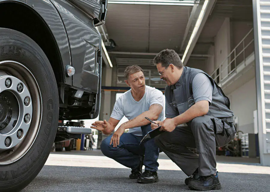 Two men crouched inspecting the front of a lorry cab